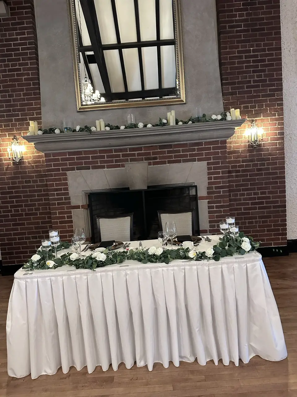 Head table beneath a candle and rose garland on a fireplace mantel