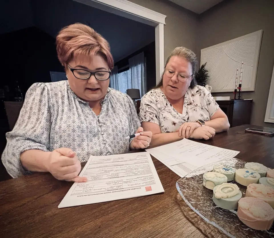 Tracey and Cindy reviewing a client's Vision Information Package at the kitchen table
